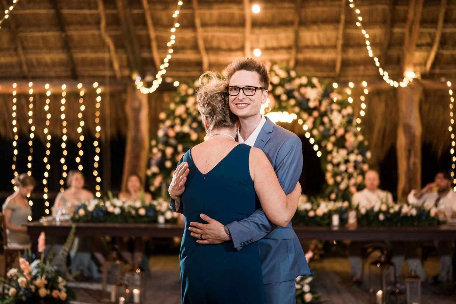 Groom shares emotional dance with mother at elegant wedding reception with string lights.