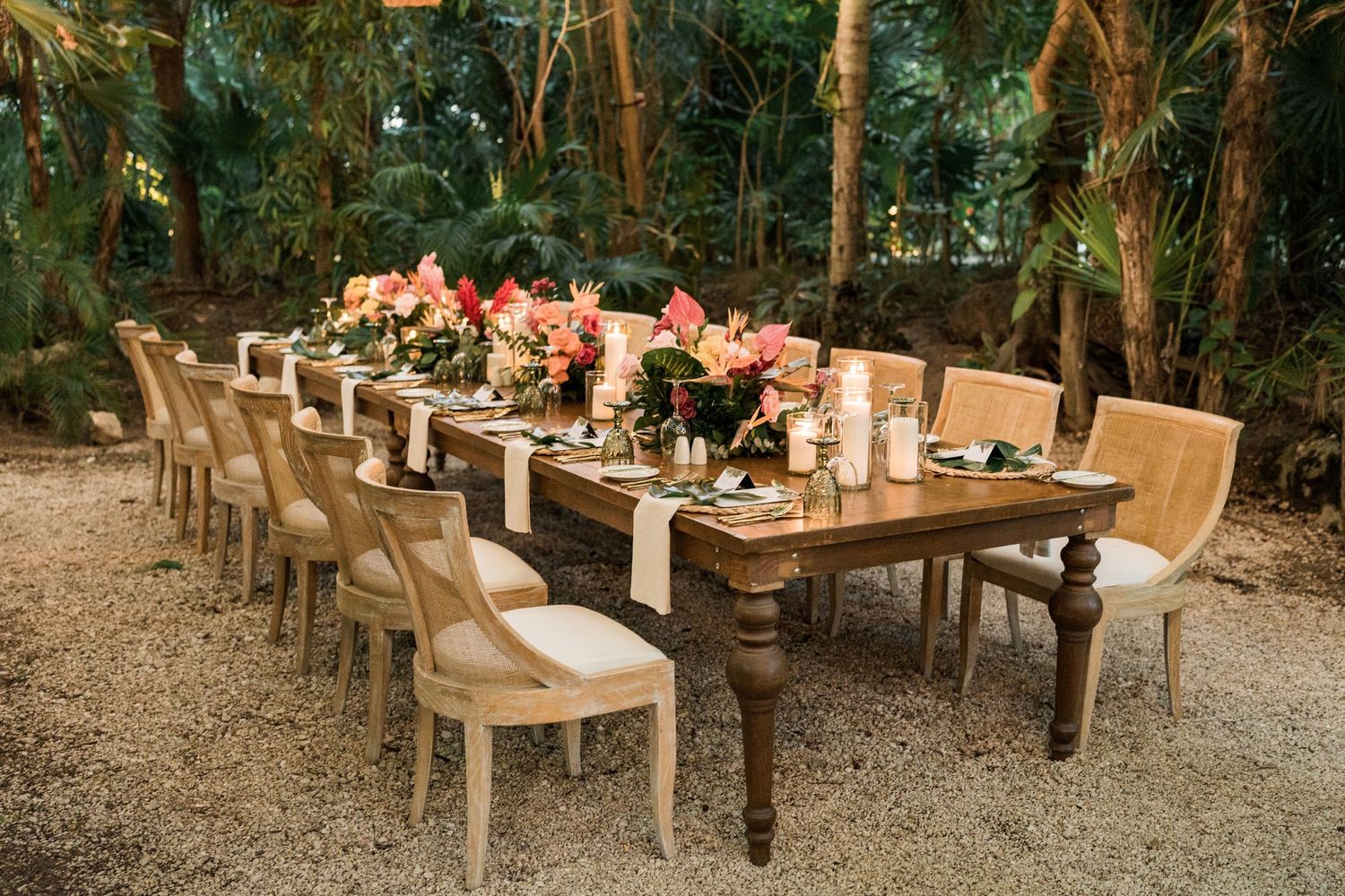 Secrets Akumal Wedding - Elegant outdoor dining table with floral centerpieces and lush tropical greenery backdrop for a wedding reception.