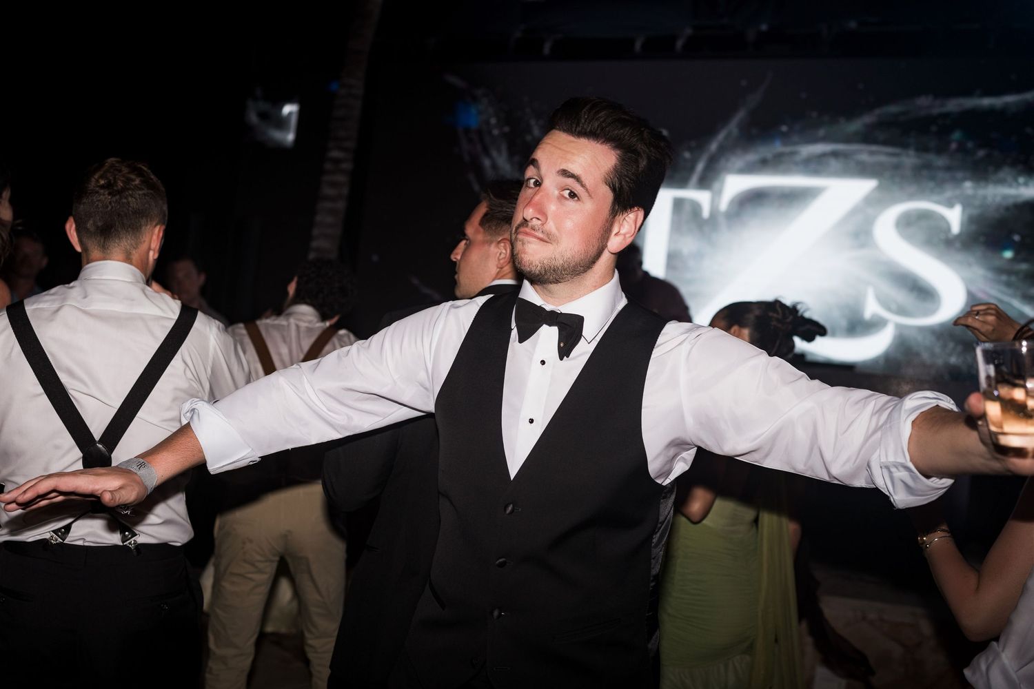 Young man in tuxedo vest and bow tie dancing with arms outstretched at a formal evening event. TRS Yucatán Hotel Wedding