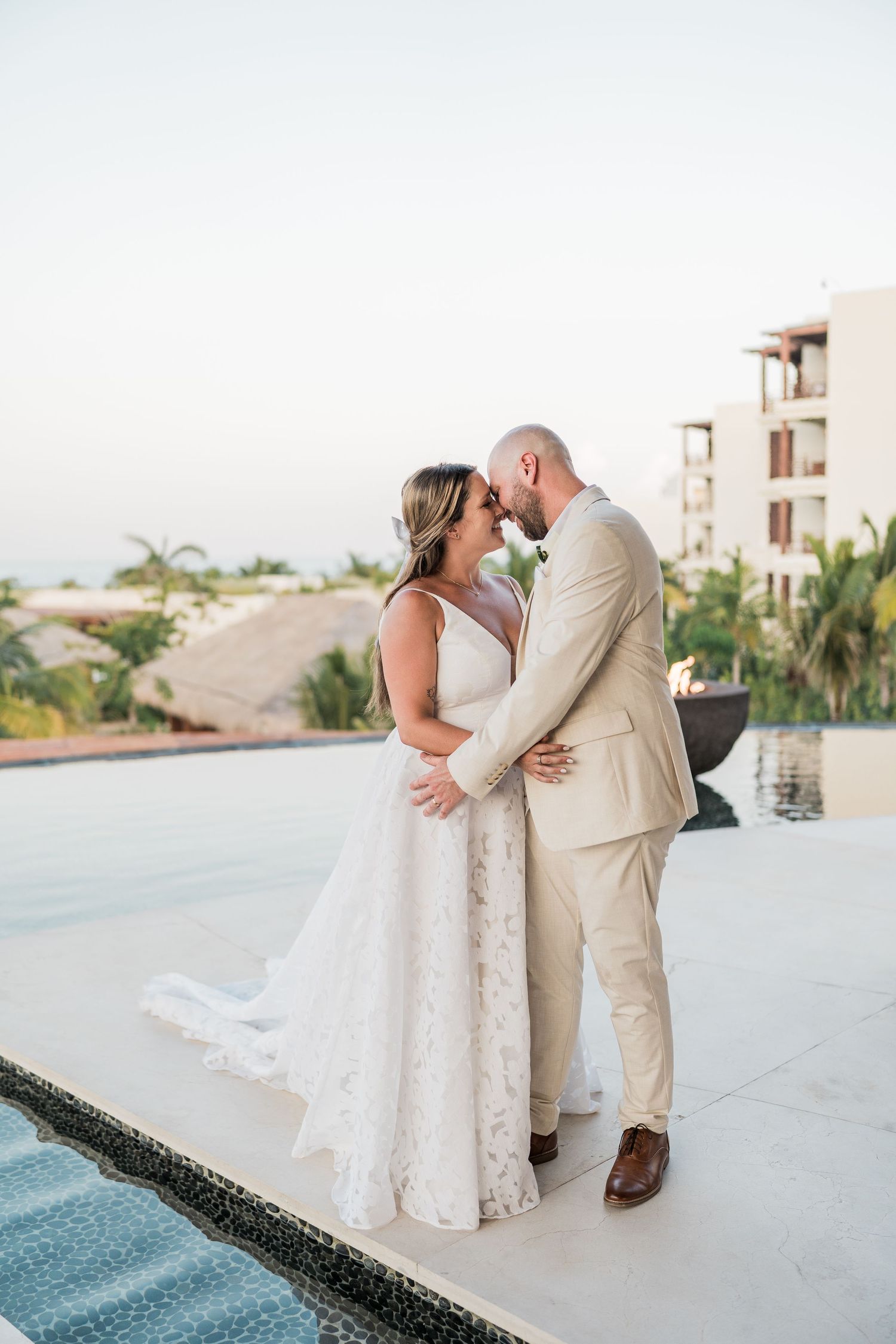 A bride and groom share a romantic moment by a pool at a tropical resort during their destination wedding.