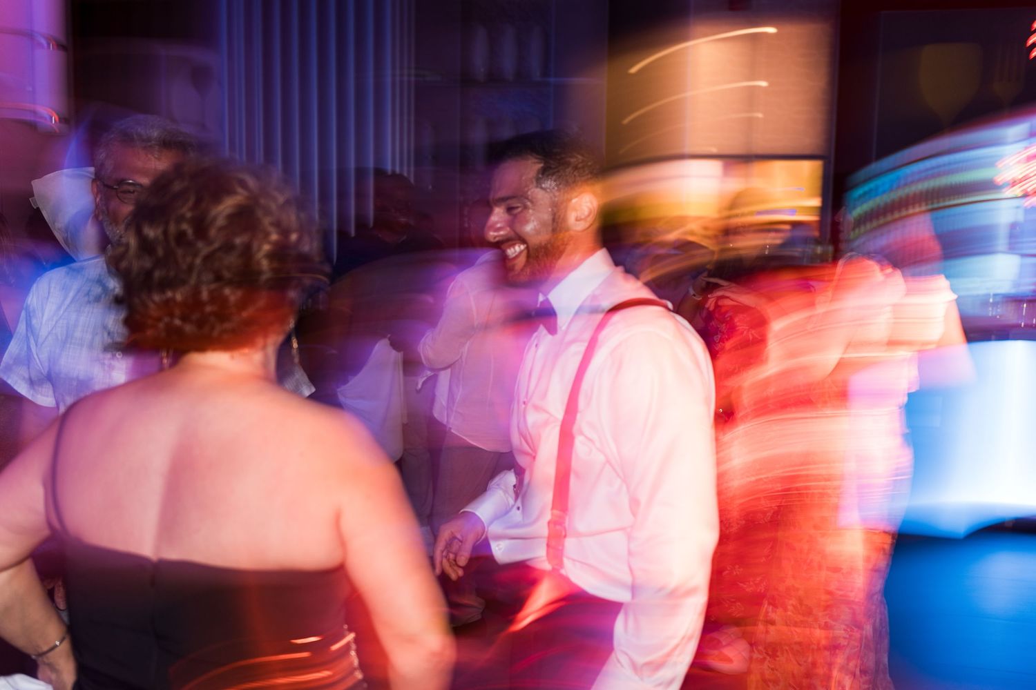 Man in white shirt with suspenders dancing energetically at a wedding reception.