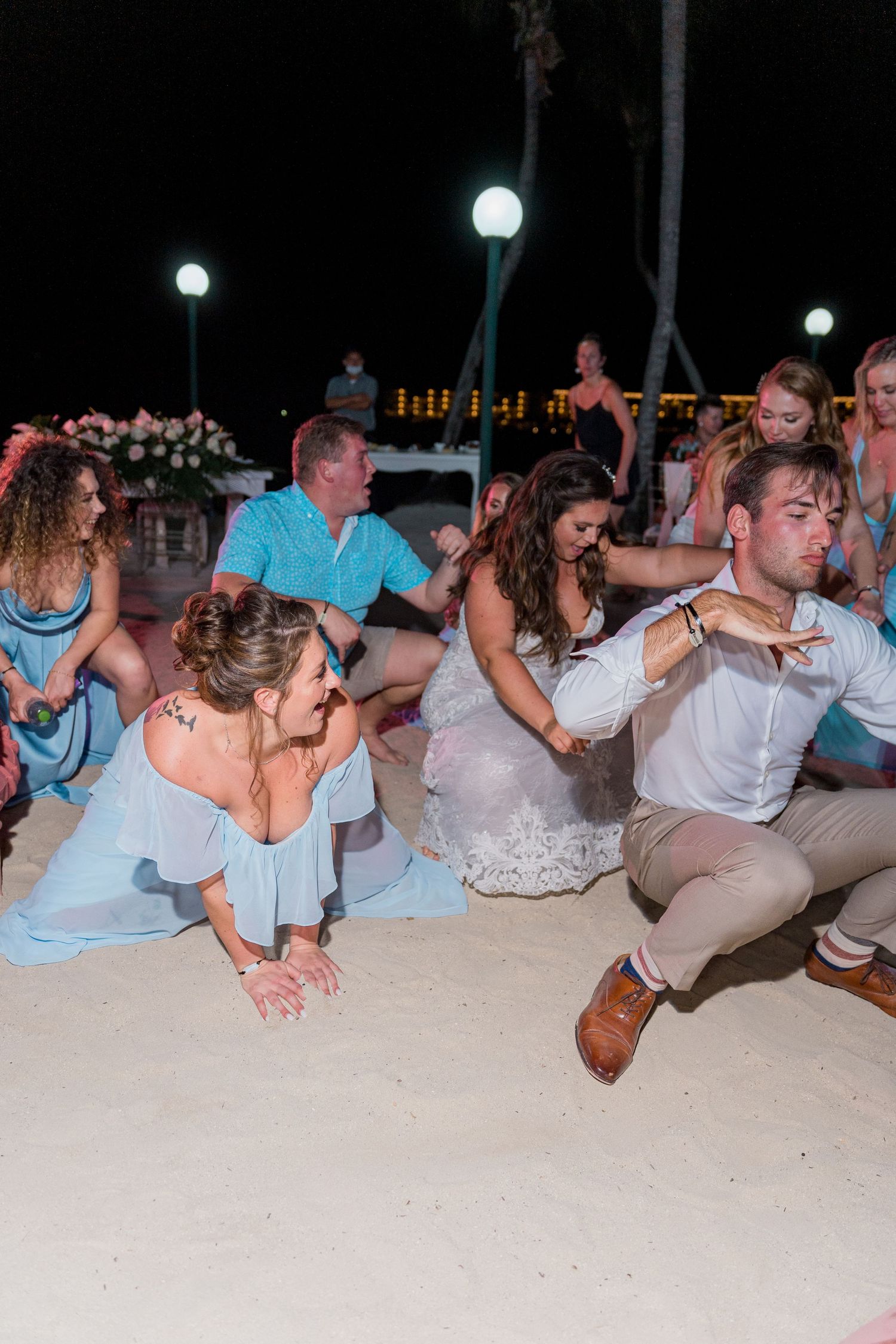 Wedding guests dancing on sandy beach at night during outdoor reception celebration.
