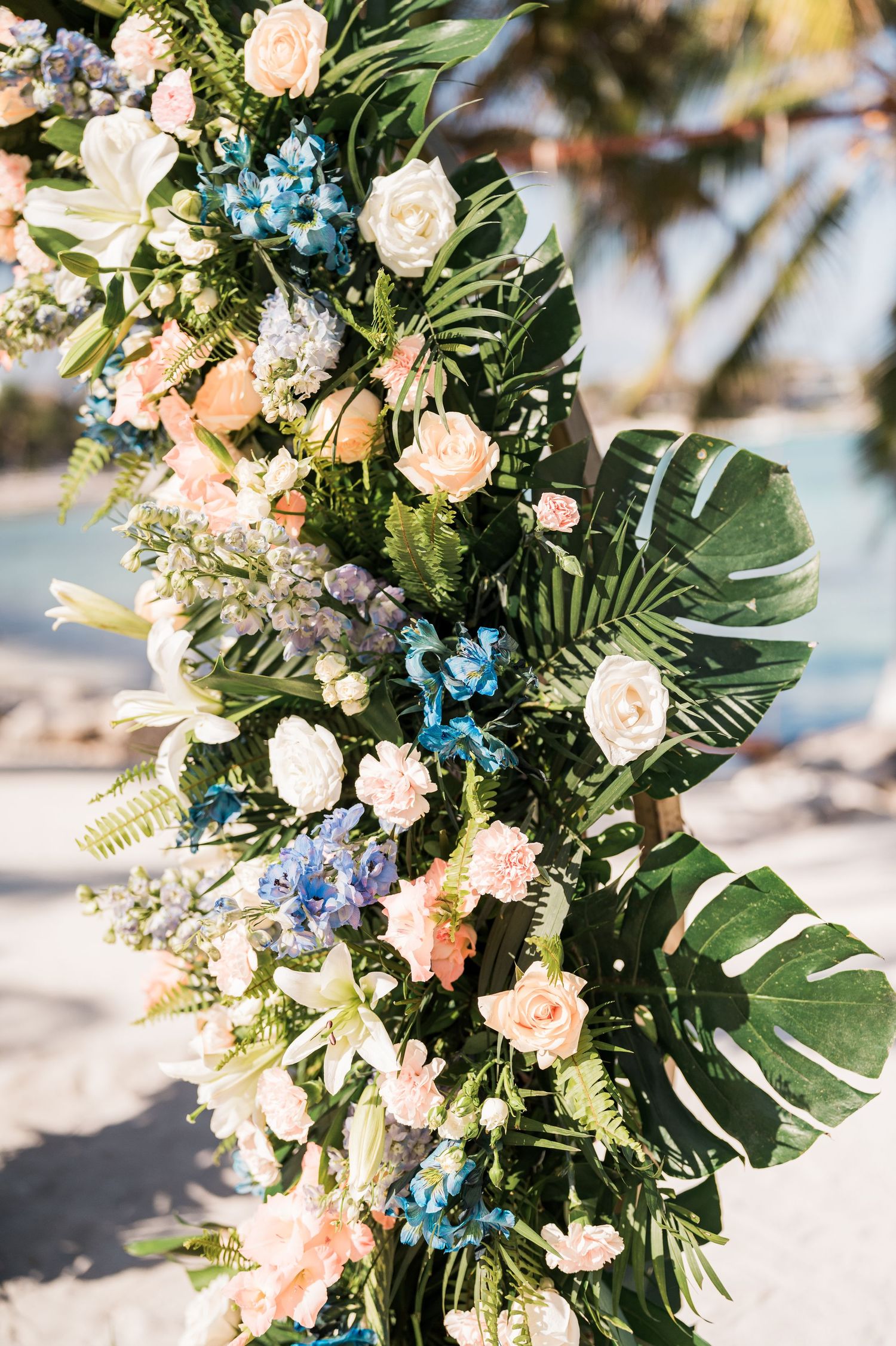 Close-up of tropical wedding arch adorned with peach, white, and blue flowers and monstera leaves.