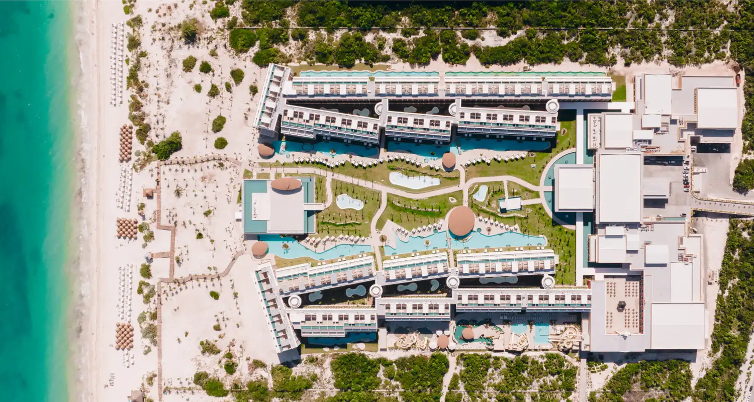 Aerial view of a luxury beachfront resort with pools, lush gardens, and turquoise ocean waters in a tropical destination.