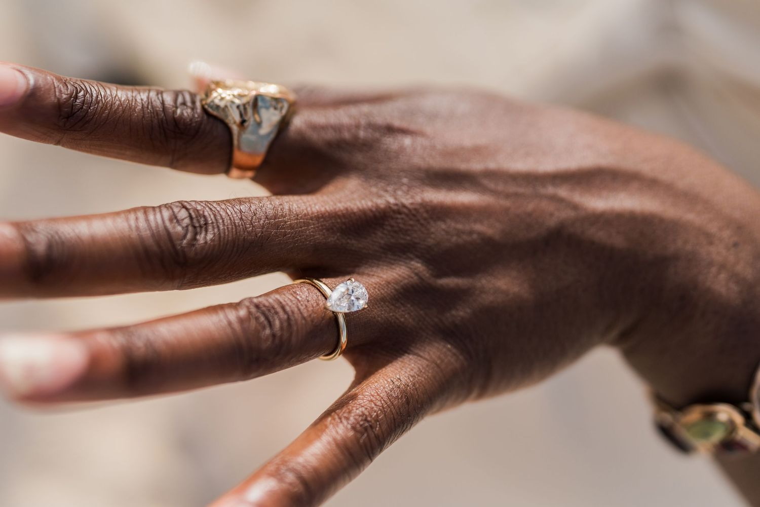 Close-up of a dark-skinned hand wearing a large diamond solitaire engagement ring and a gold signet ring.