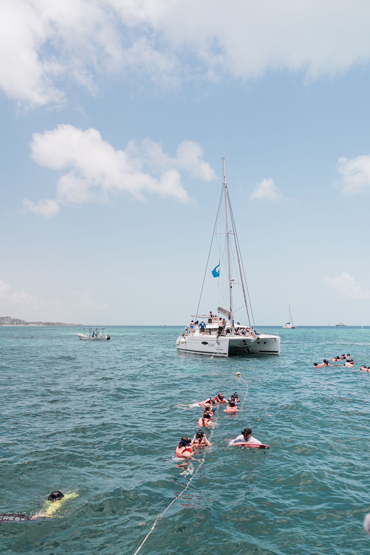 Riviera Maya Multi Day wedding - Tourists snorkeling in turquoise Caribbean waters near a white catamaran sailboat on a sunny day.