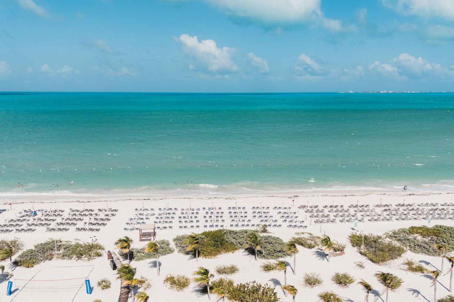 Aerial view of a pristine white sand beach with turquoise ocean waters and rows of beach chairs under blue skies.