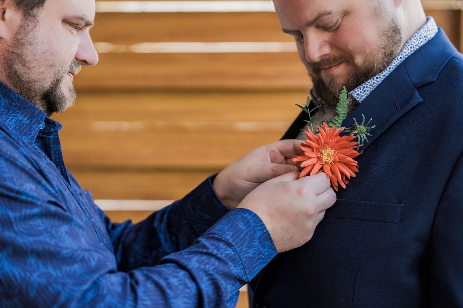 Secrets Akumal Wedding - Man pinning an orange chrysanthemum boutonniere on a groom in a navy suit before a wedding ceremony.
