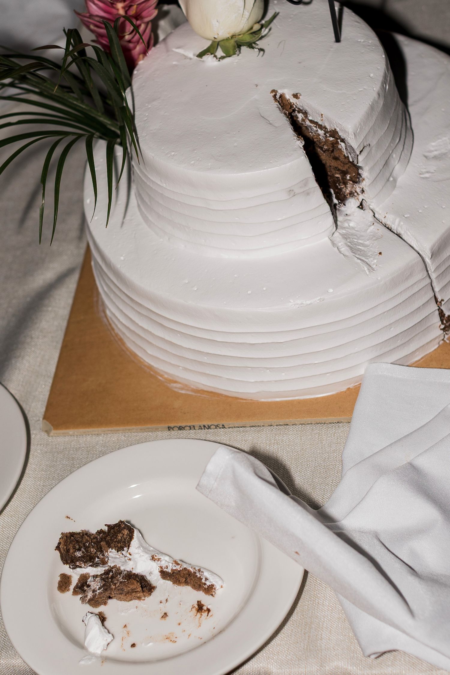 Two-tier white frosted wedding cake with a slice cut out, revealing chocolate interior, displayed on a wooden board.