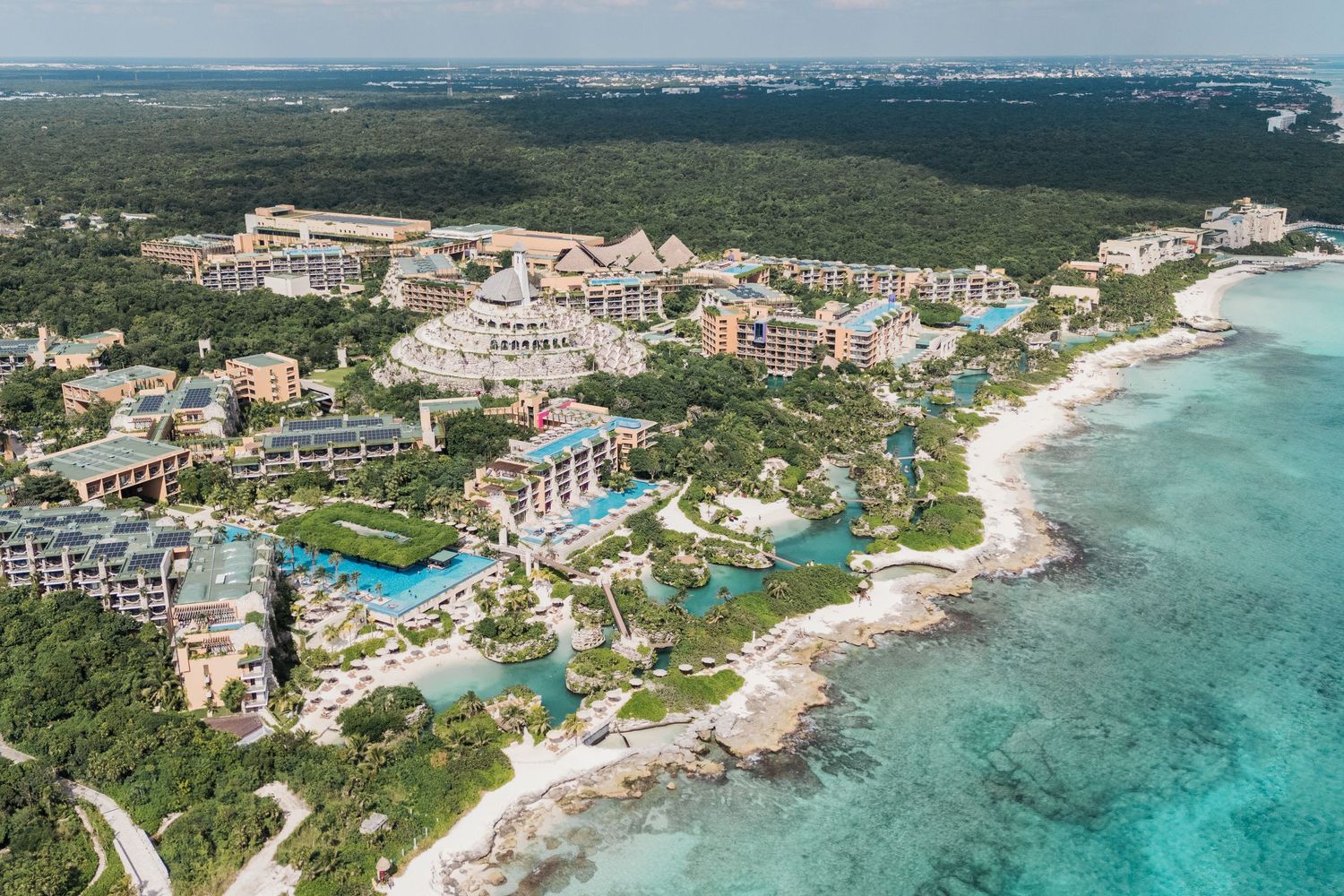 Xcaret Arte Wedding - Aerial view of a luxury beachfront resort nestled among lush tropical jungle along the turquoise Caribbean coastline.