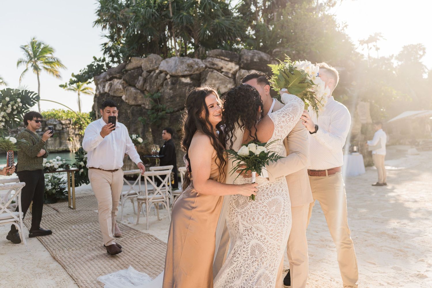 Xcaret Arte Wedding - Bride and groom share a joyful hug with guests at an outdoor beach wedding ceremony surrounded by tropical greenery.