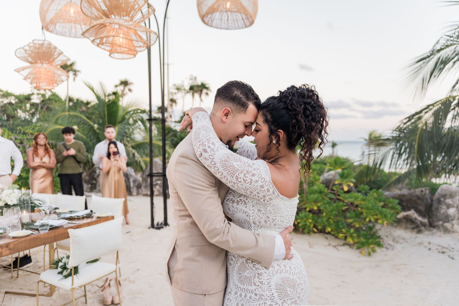 Xcaret Arte Wedding - Couple shares first dance on beach at sunset wedding ceremony with guests watching and tropical decor.