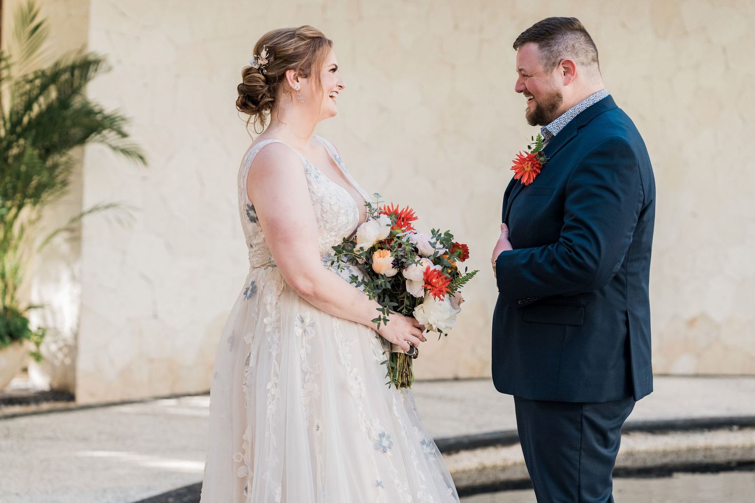 Secrets Akumal Wedding - Bride in lace gown holds colorful bouquet facing groom in navy suit during outdoor wedding first look.