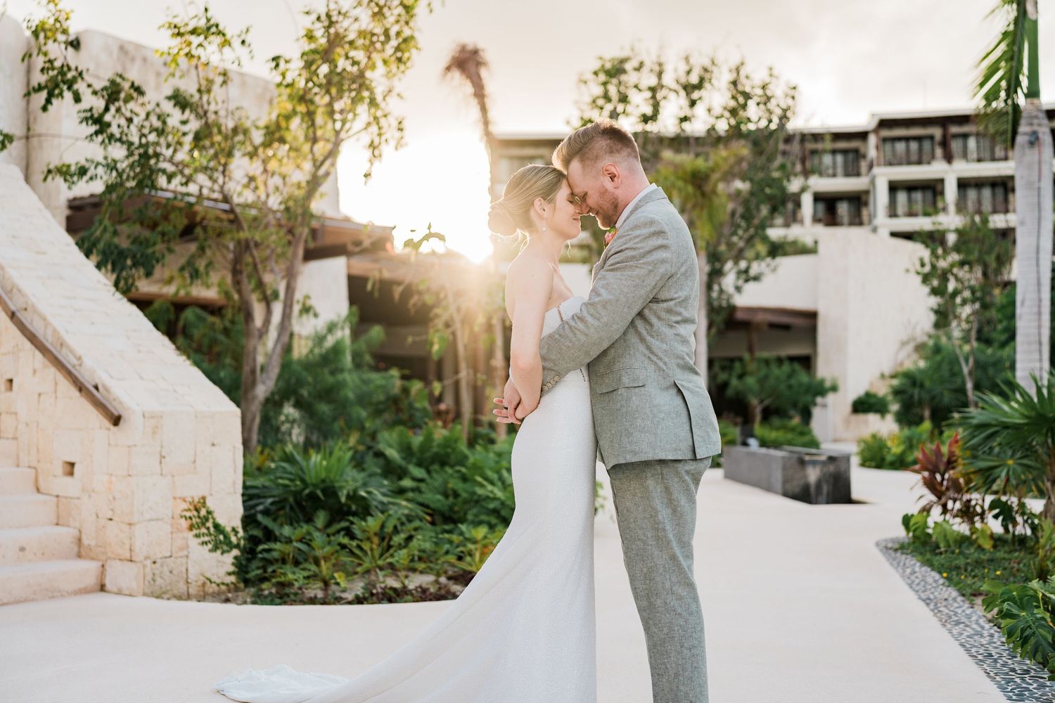Bride and groom share romantic sunset embrace in lush garden at elegant resort wedding venue.