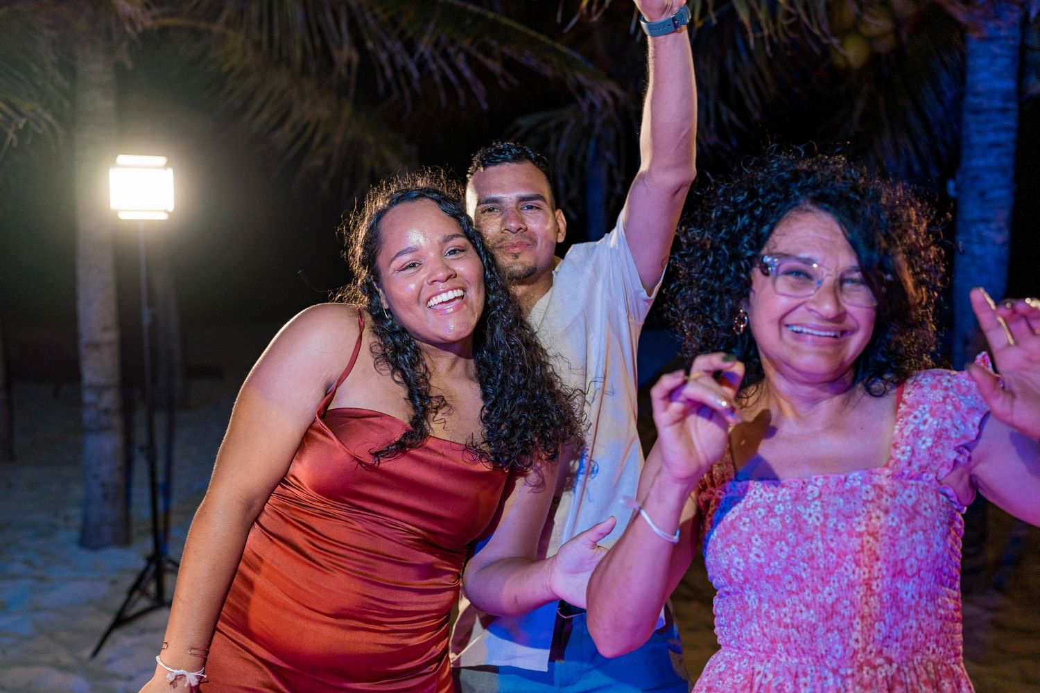 Three guests smiling and dancing at outdoor beach wedding reception at night.