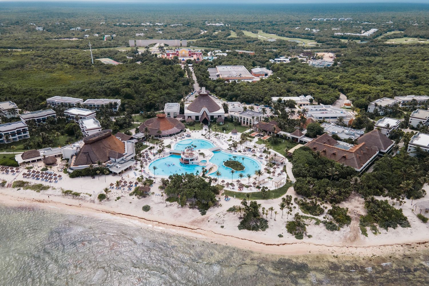 Aerial view of tropical resort featuring large pool, beach access, and surrounding jungle.