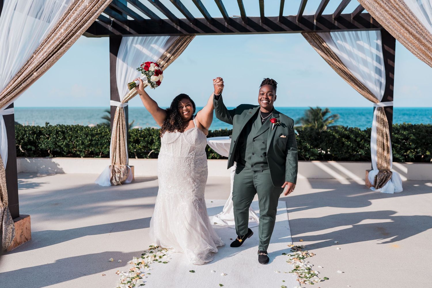 Joyful newlyweds raise hands in celebration after beach destination wedding ceremony.