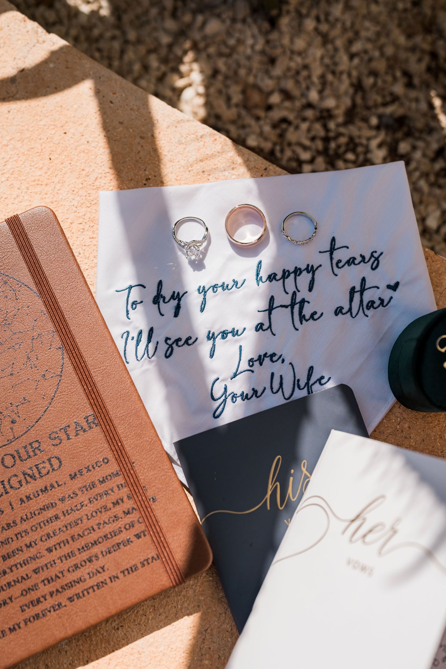 Wedding flat lay with rings, vow books, and a handwritten note reading To dry your happy tears, I'll see you at the altar, Love Your Wife.