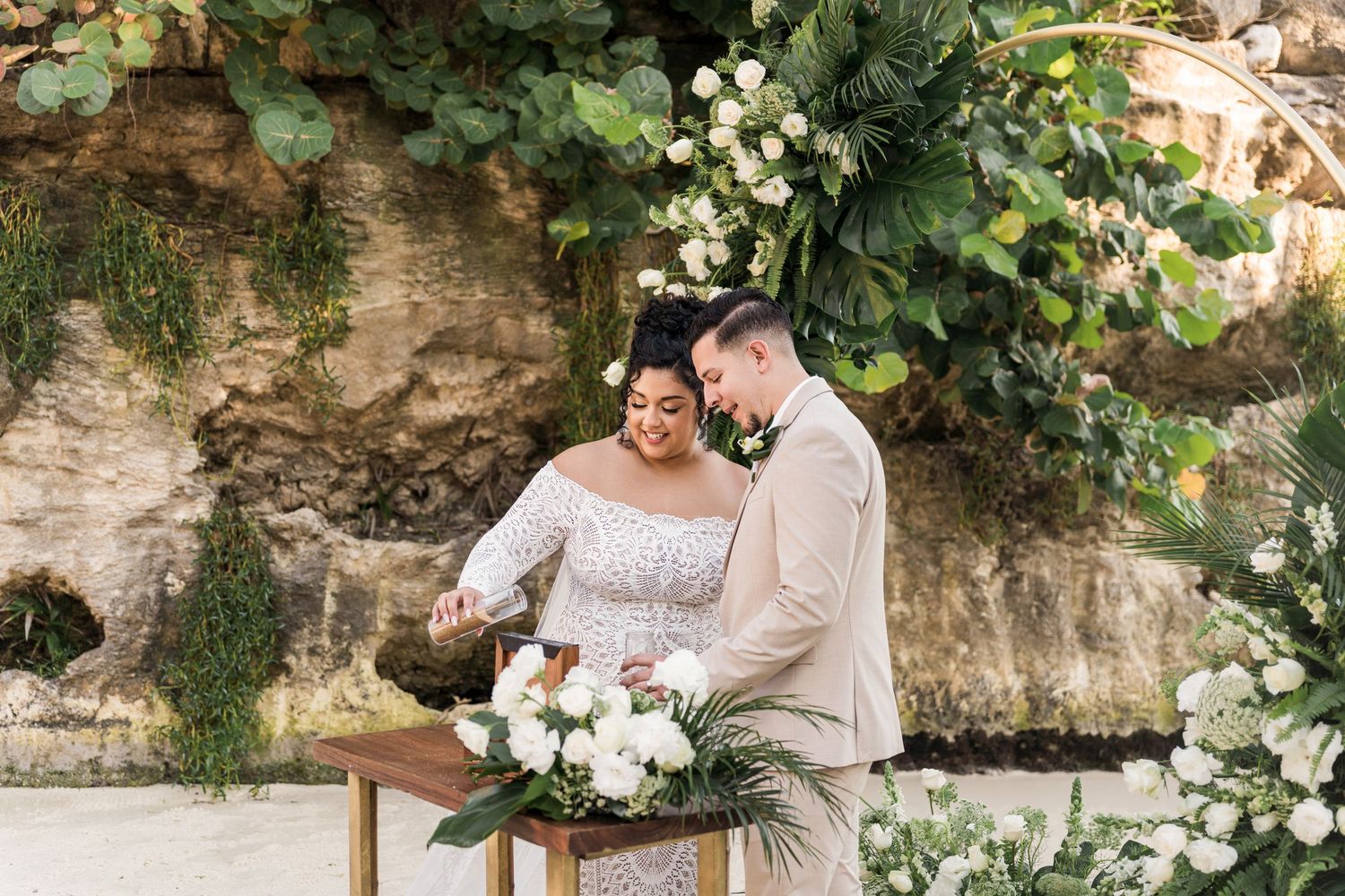 Xcaret Arte Wedding - Bride and groom signing wedding documents at elegant outdoor ceremony with lush greenery and white floral backdrop.
