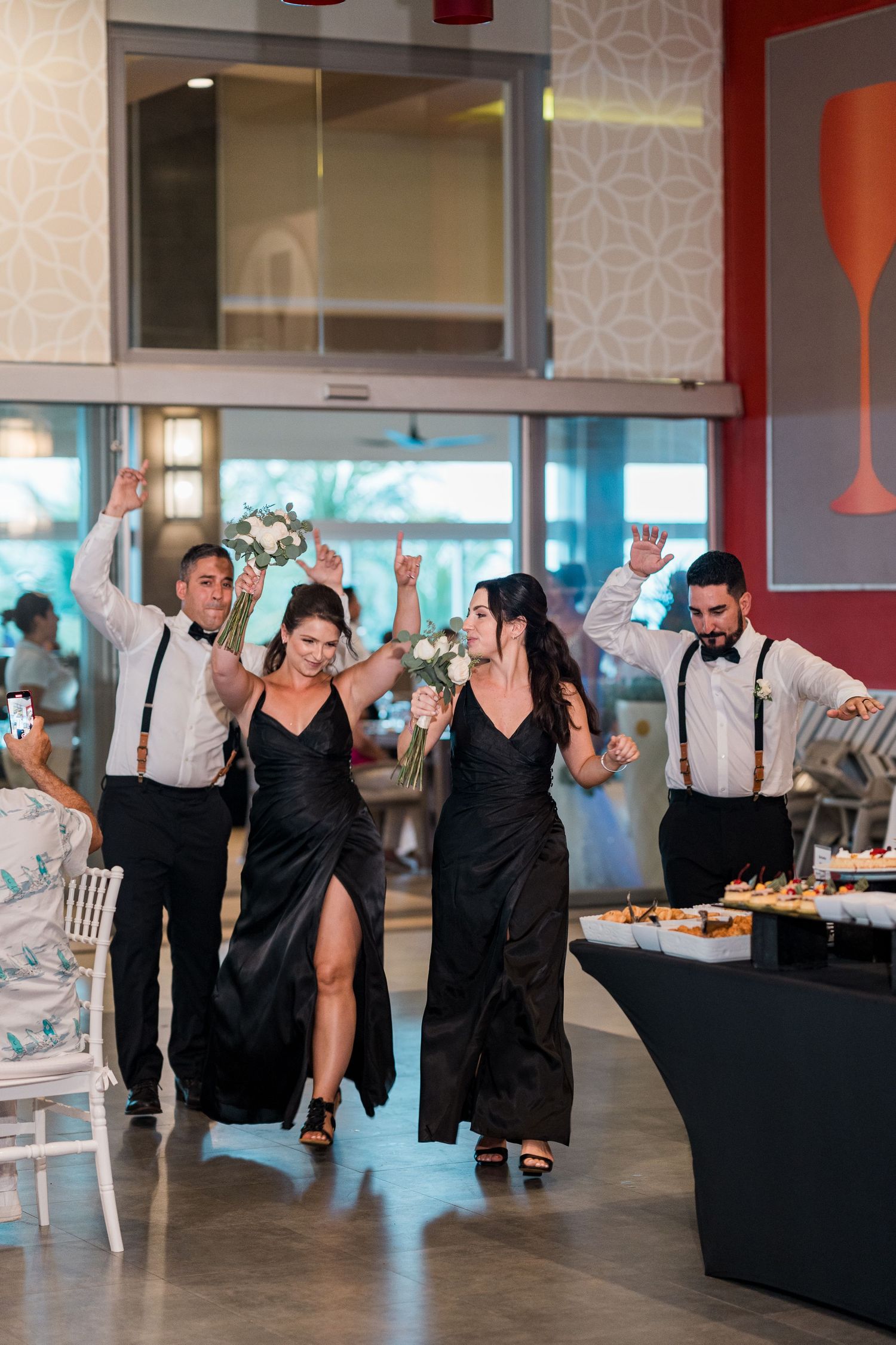 Bridesmaids in black gowns and groomsmen in suspenders make a celebratory entrance at wedding reception.