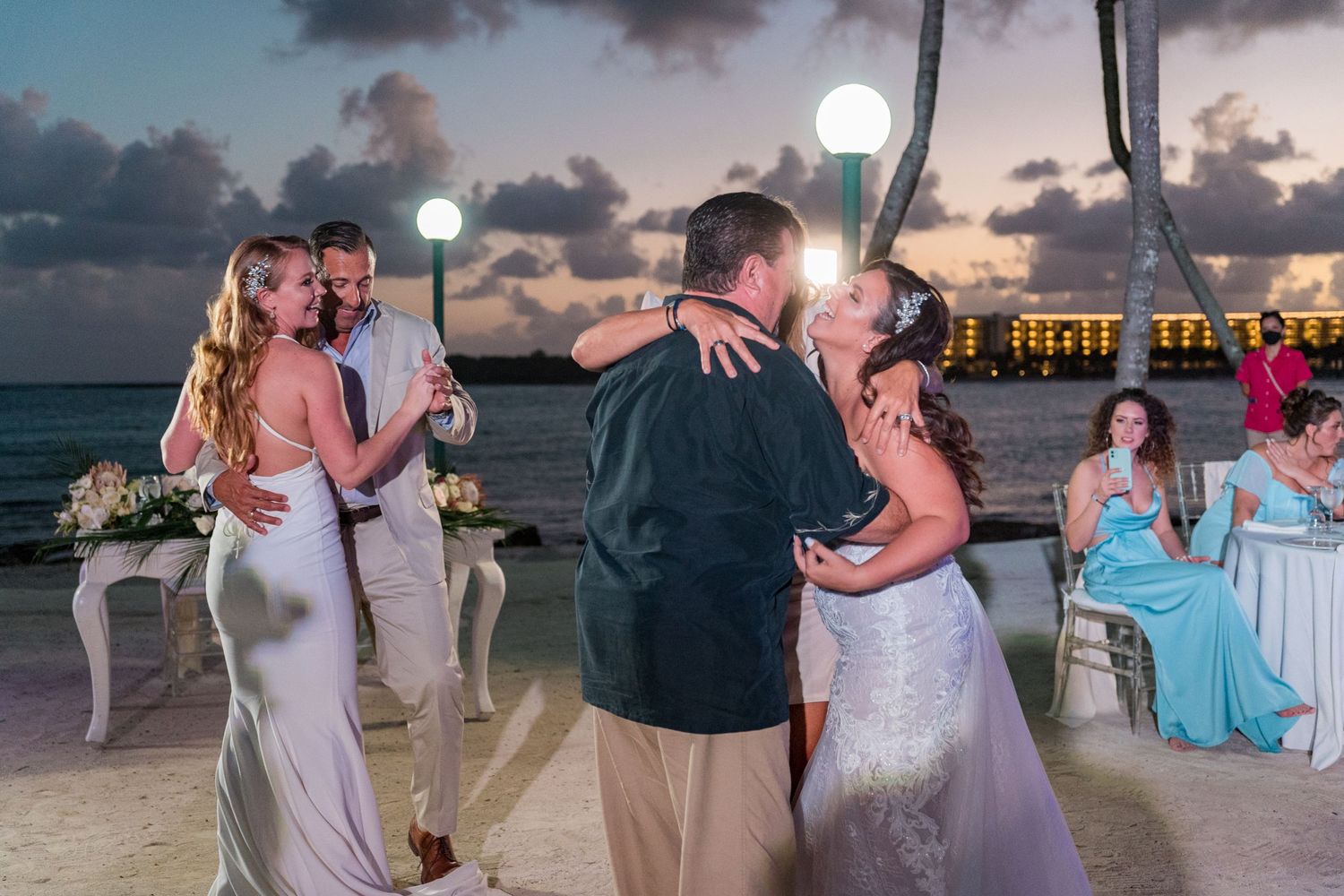 Two brides kissing partners during romantic beach wedding reception dances at sunset.