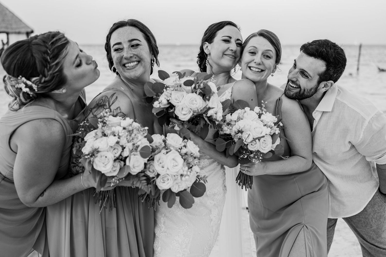 Black and white photo of bride and bridesmaids hugging on beach.