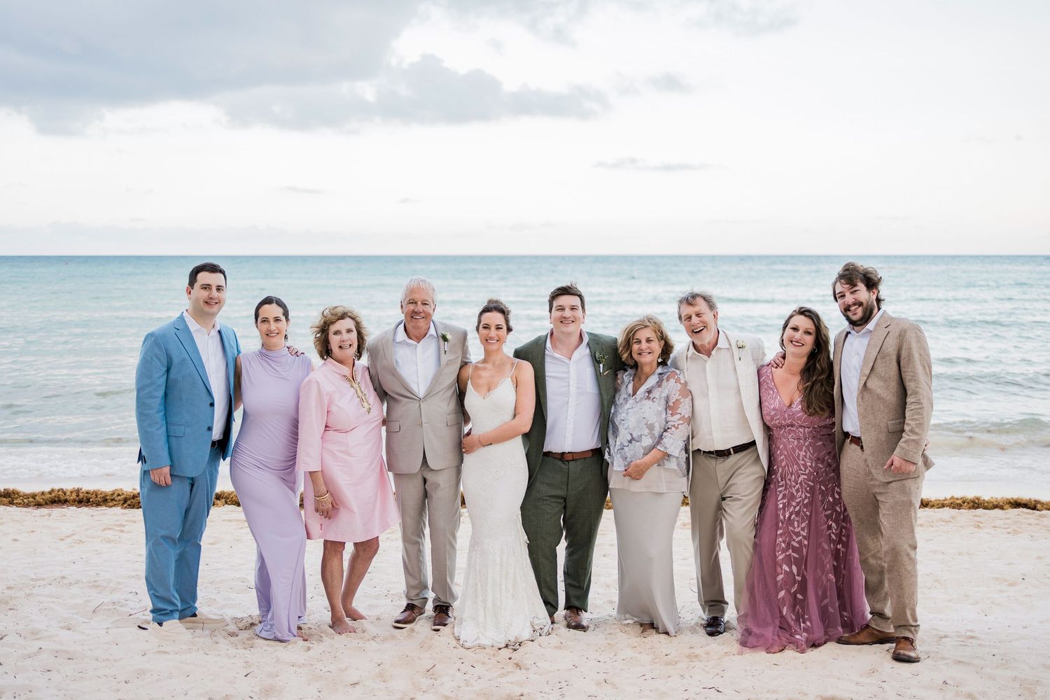 Wedding party posing together on a sandy beach with ocean backdrop, dressed in elegant formal attire.