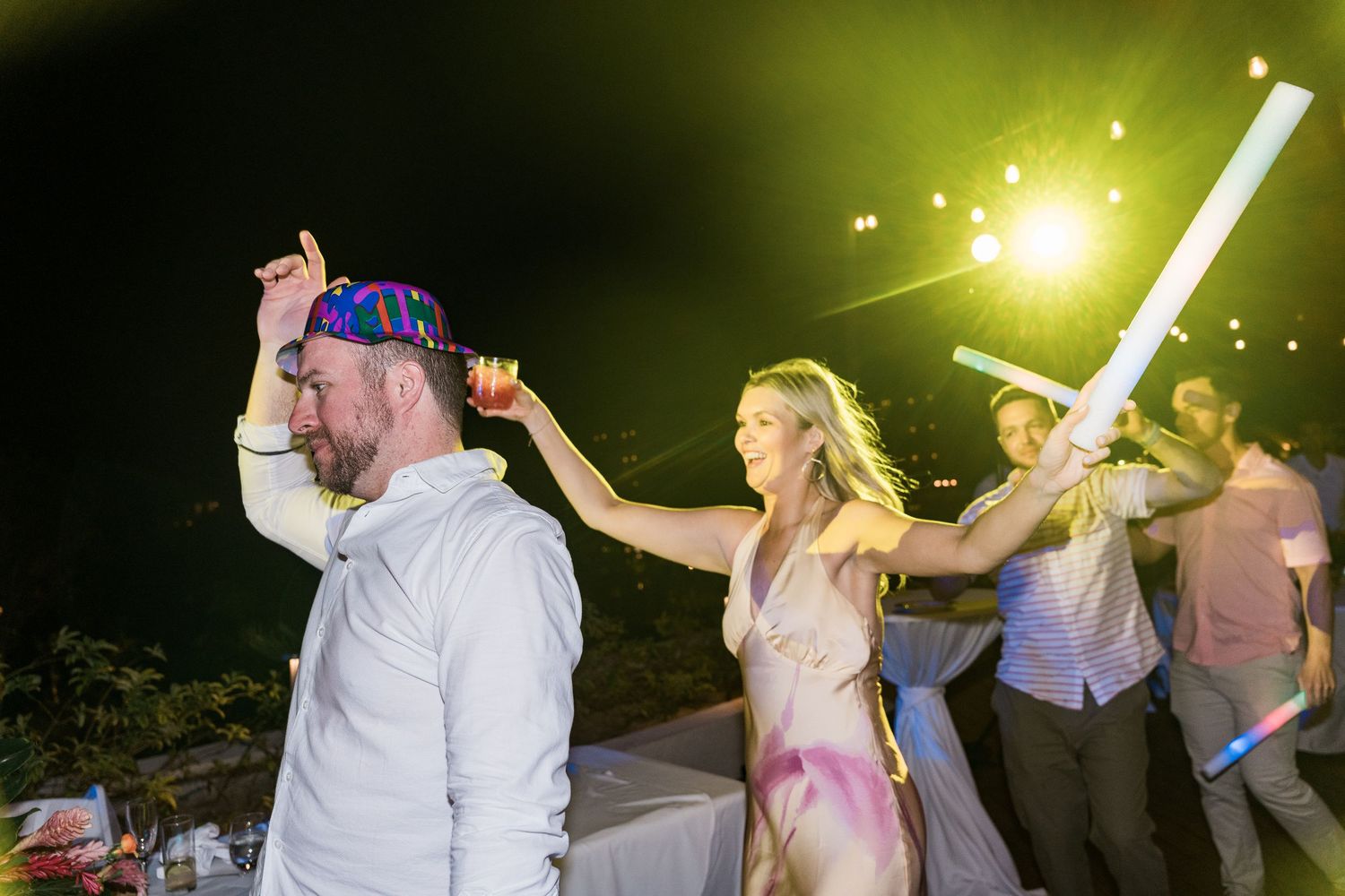 Guests dancing at an outdoor night wedding reception with glow sticks and colorful lights.