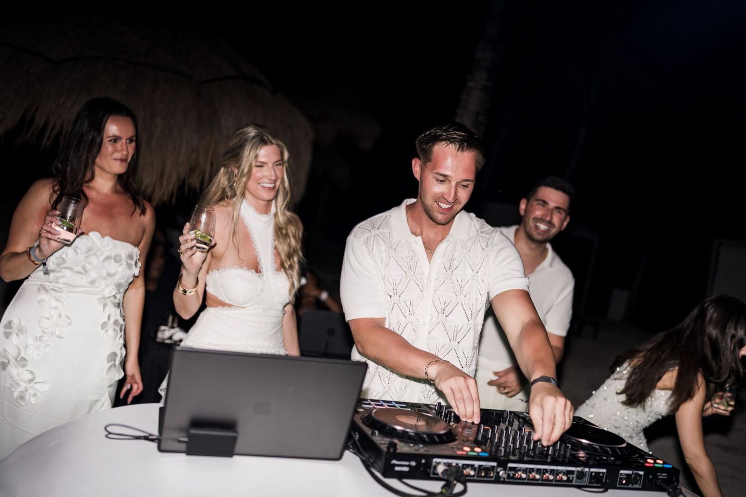 DJ performing at outdoor wedding reception while guests in white attire celebrate at night.