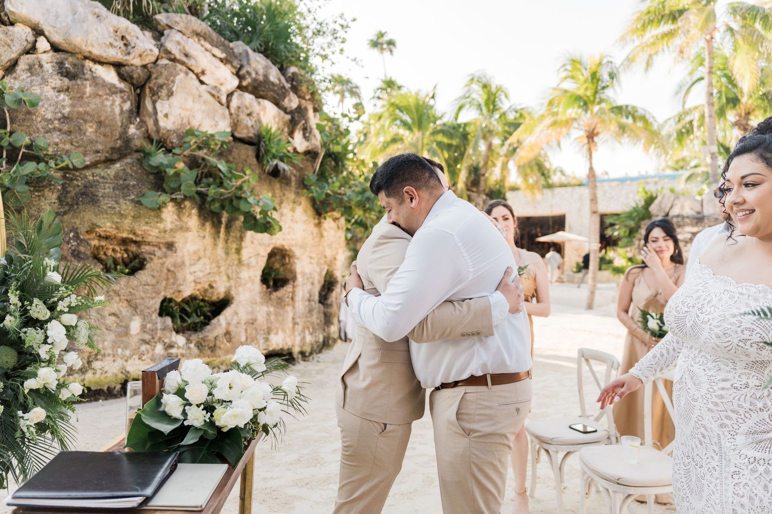 Xcaret Arte Wedding - Two grooms share an emotional hug during an outdoor beach wedding ceremony