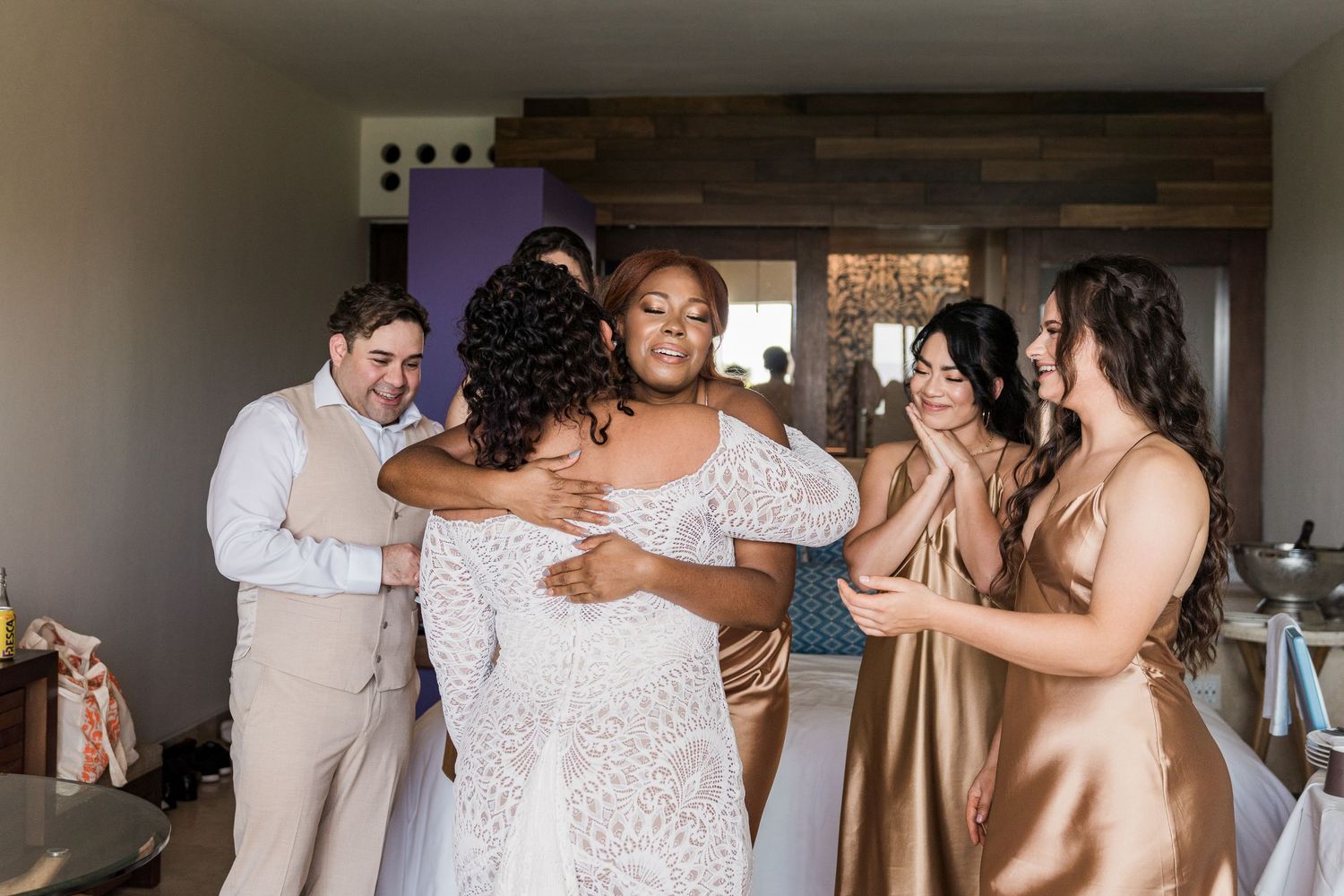 Xcaret Arte Wedding - Bride in lace wedding gown surrounded by bridesmaids in gold dresses and groomsmen sharing a joyful group hug.