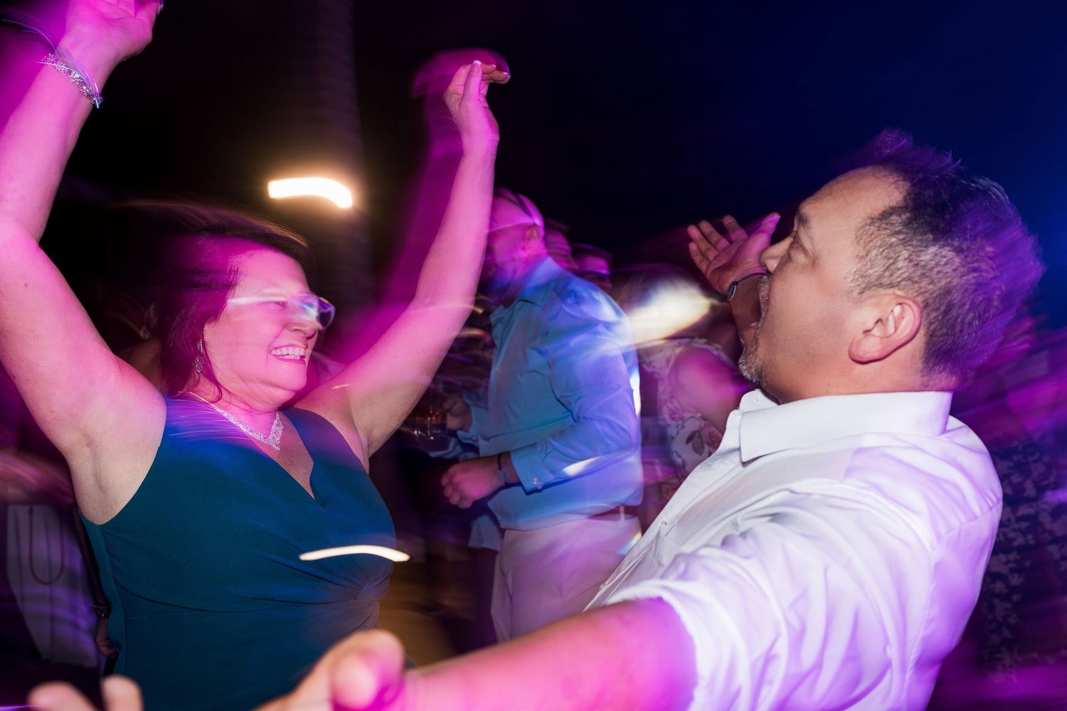 Couple dancing energetically at a lively party under colorful purple and pink lights.