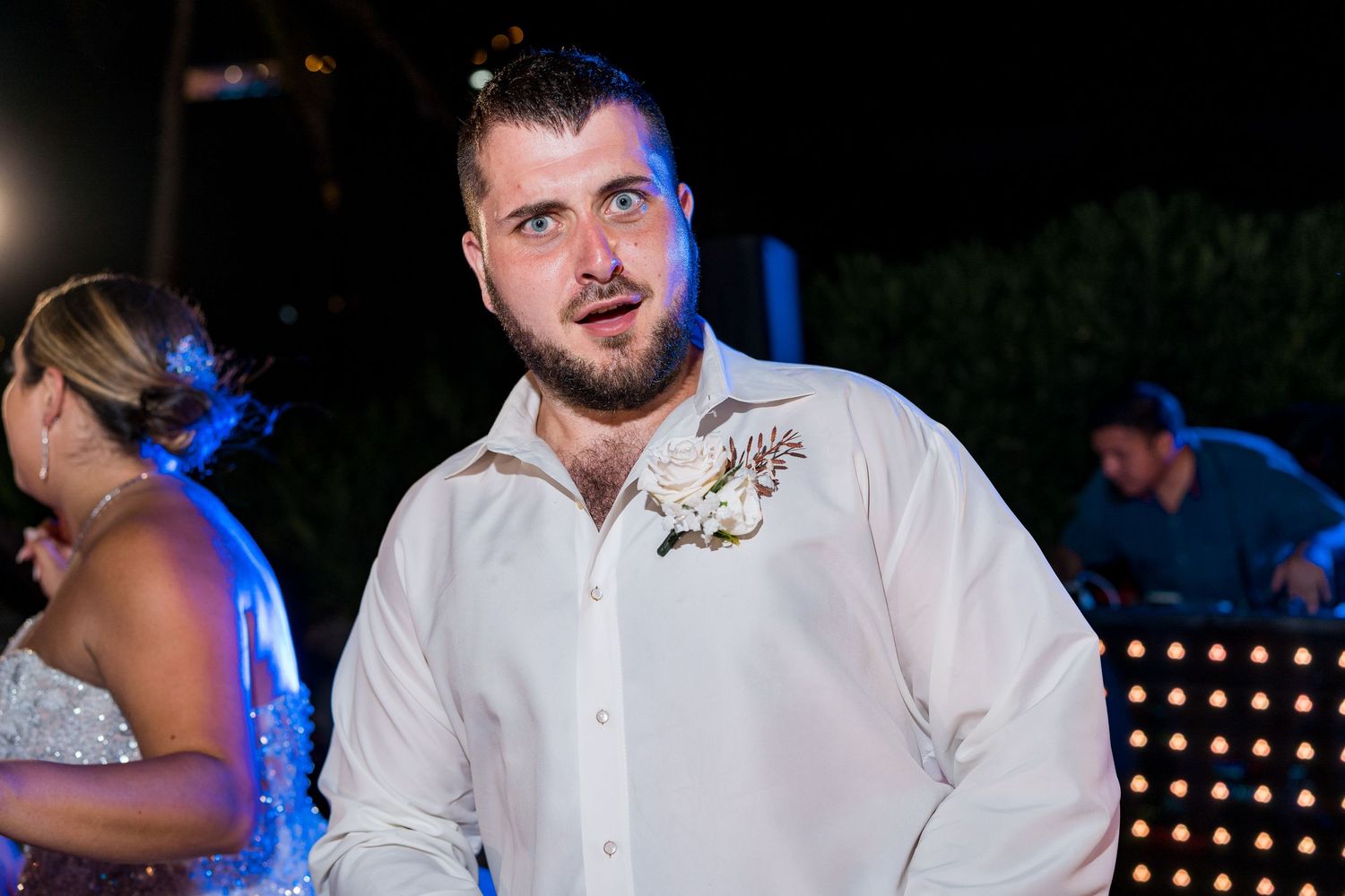 Groomsman in white shirt with floral boutonniere at outdoor beach wedding reception.