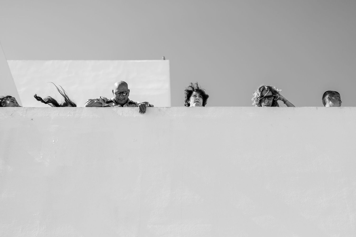 Black and white photo of wedding guests peeking over white wall.