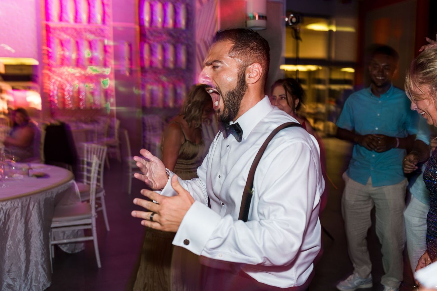 Excited man in suspenders and bow tie celebrating at a wedding reception.