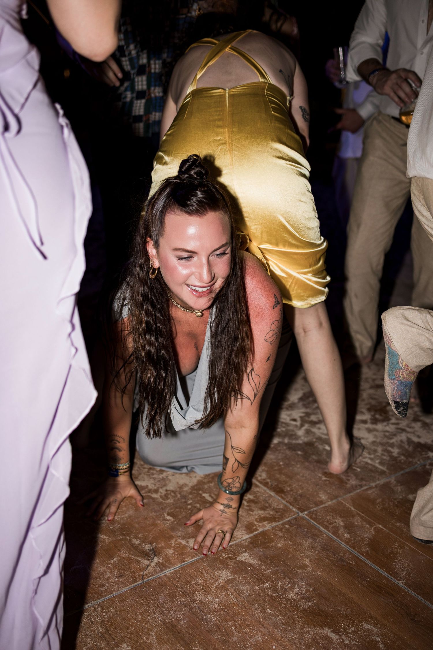 Woman with tattoos dancing energetically on a tiled dance floor at a party, wearing a gray top.