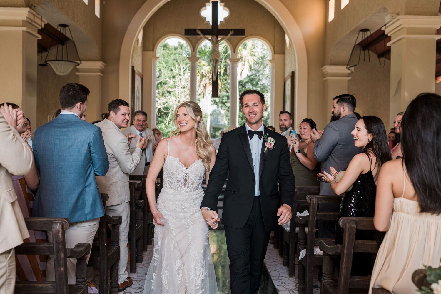 Bride and groom walk down the aisle hand in hand after wedding ceremony in elegant chapel.