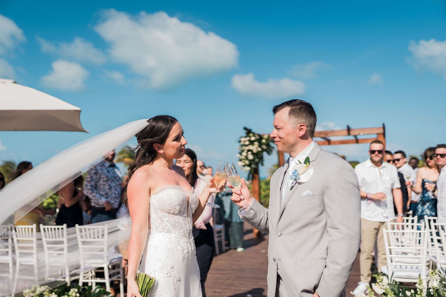 Bride and groom toasting champagne glasses after outdoor wedding ceremony under blue sky. grand palladium costa mujeres wedding