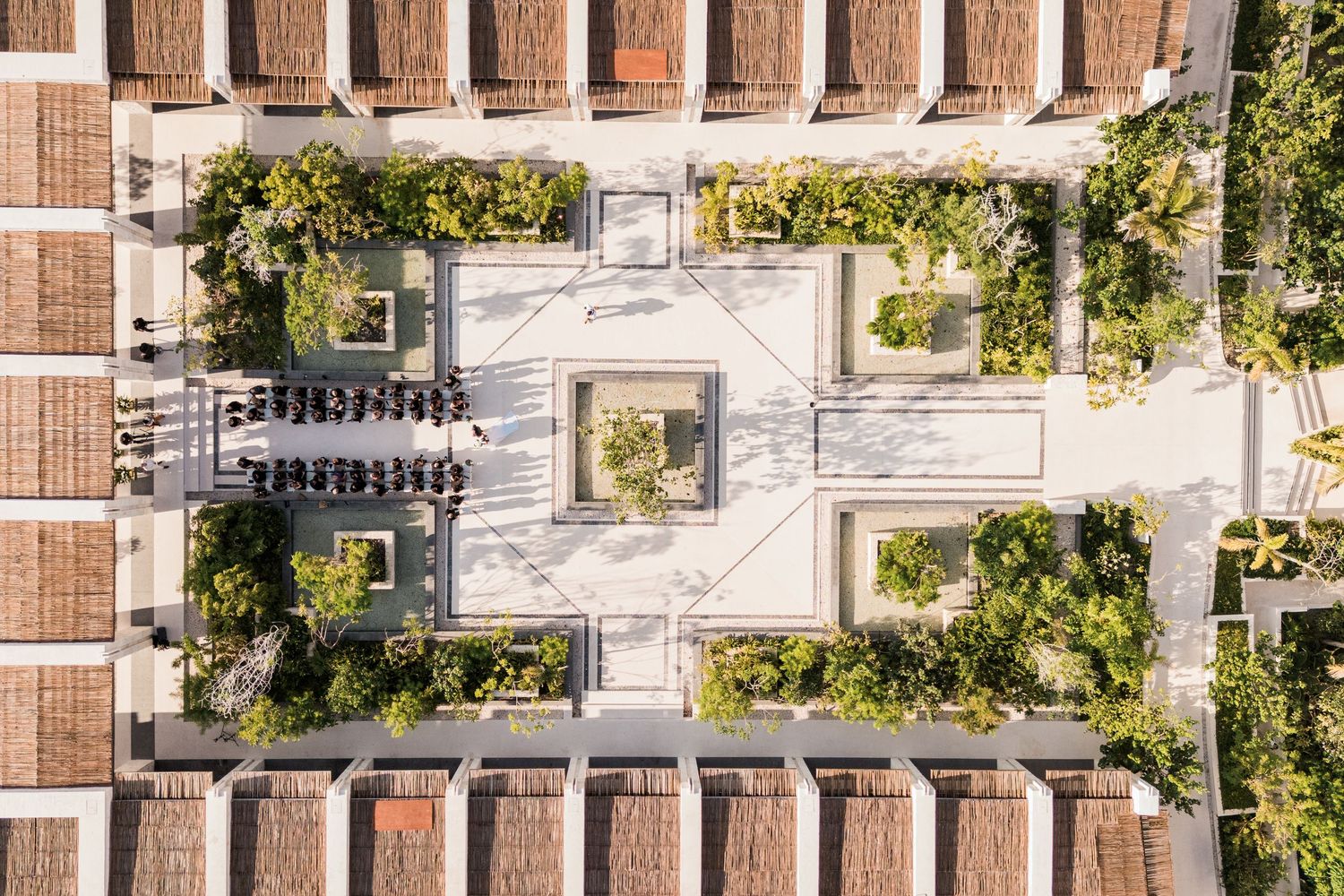 Aerial view of a symmetrical courtyard with lush greenery, terracotta rooftops, and geometric pathways in a modern architectural complex.