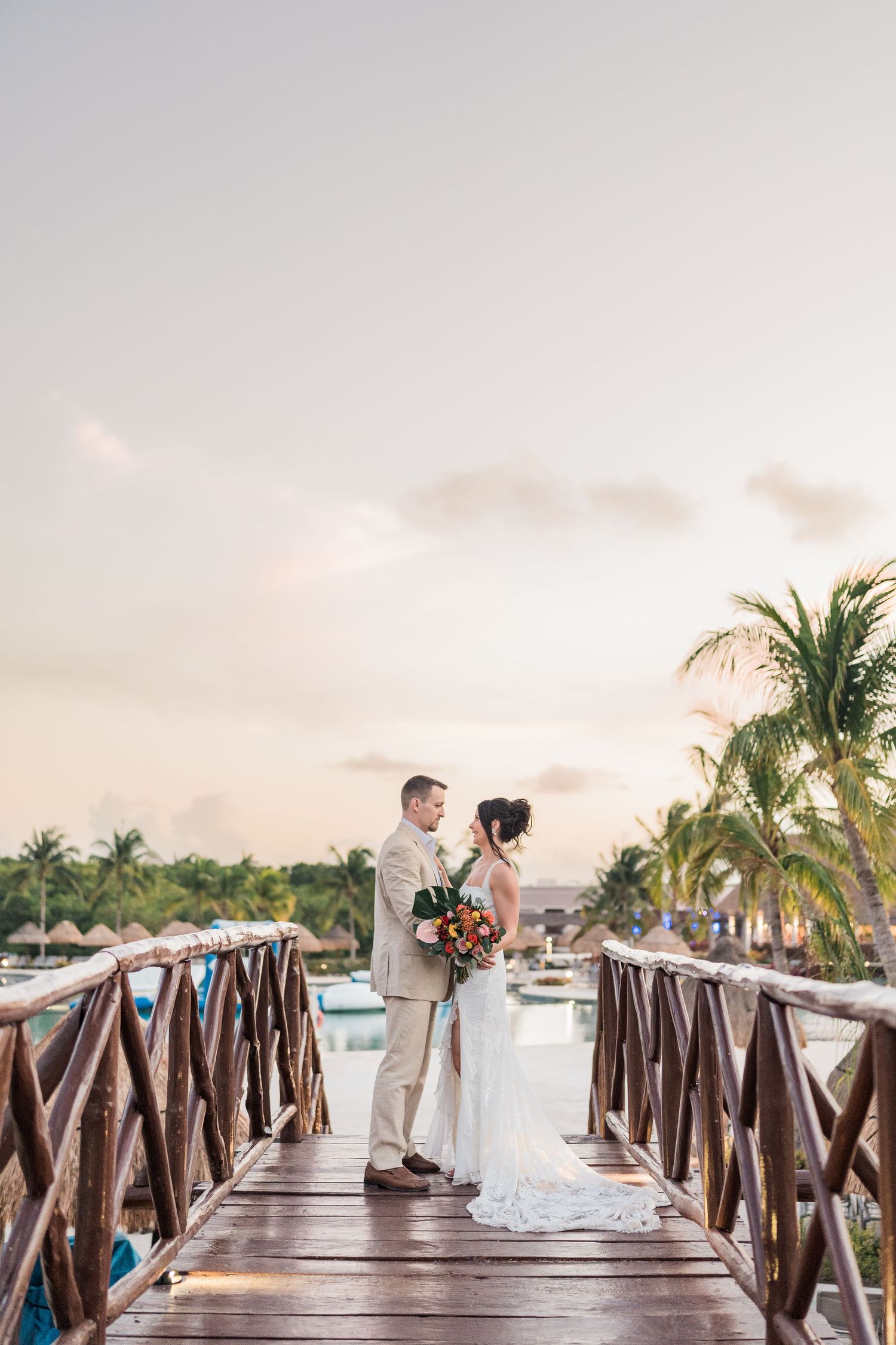 Puerto Vallarta Wedding Photo4rapherBride and groom stand on a wooden pier at sunset at a tropical resort.