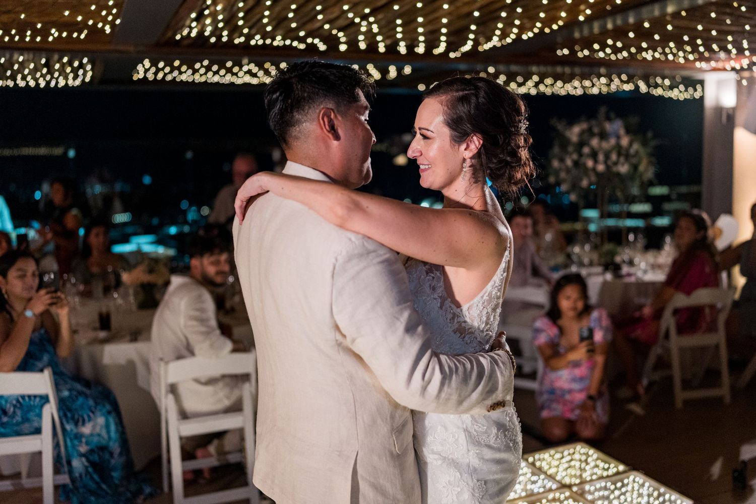 Bride and groom share their first dance under twinkling string lights at their wedding reception.