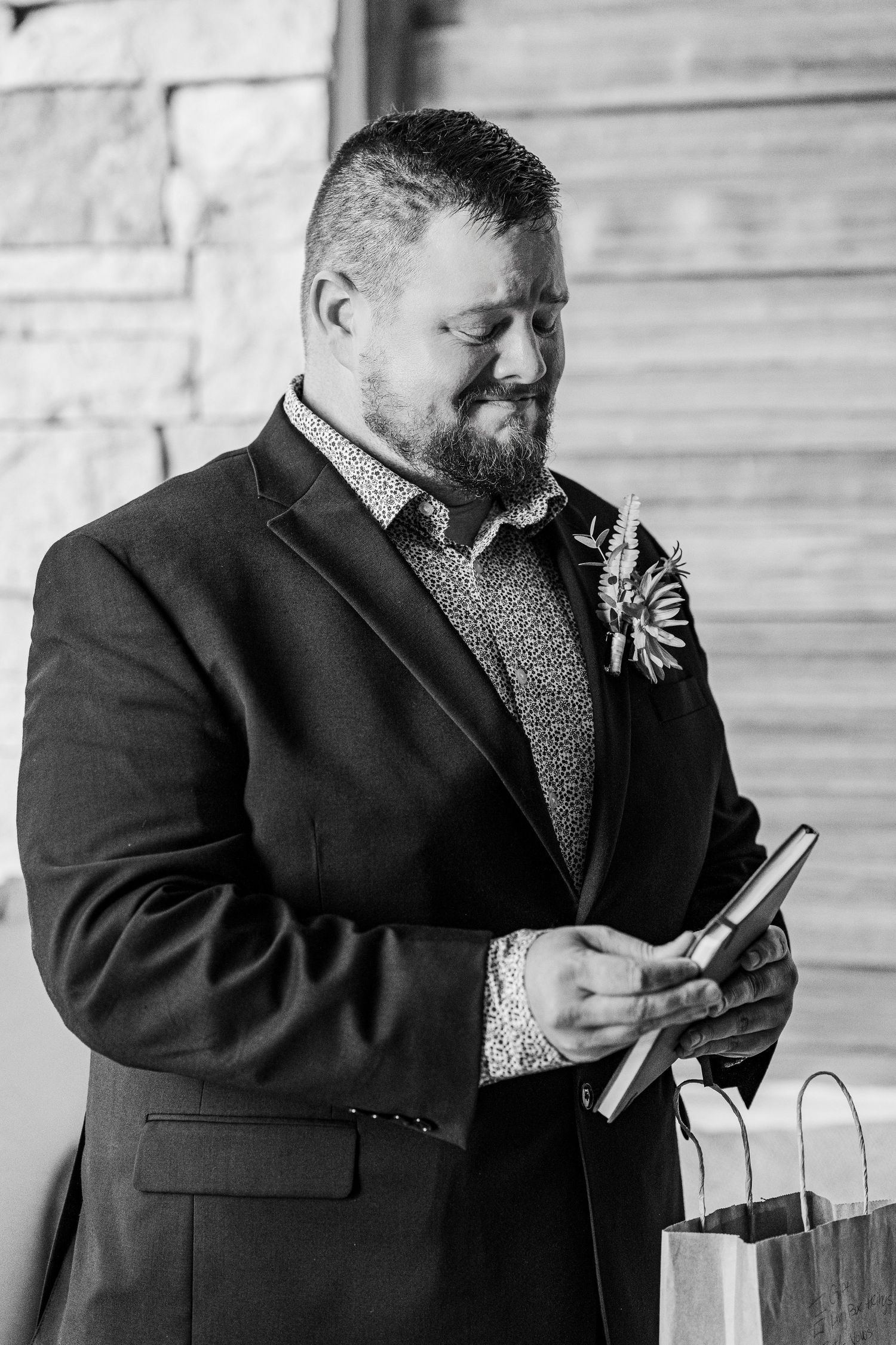 Secrets Akumal Wedding - Black and white photo of a bearded groom in a suit with boutonniere, smiling while reading a card at his wedding.
