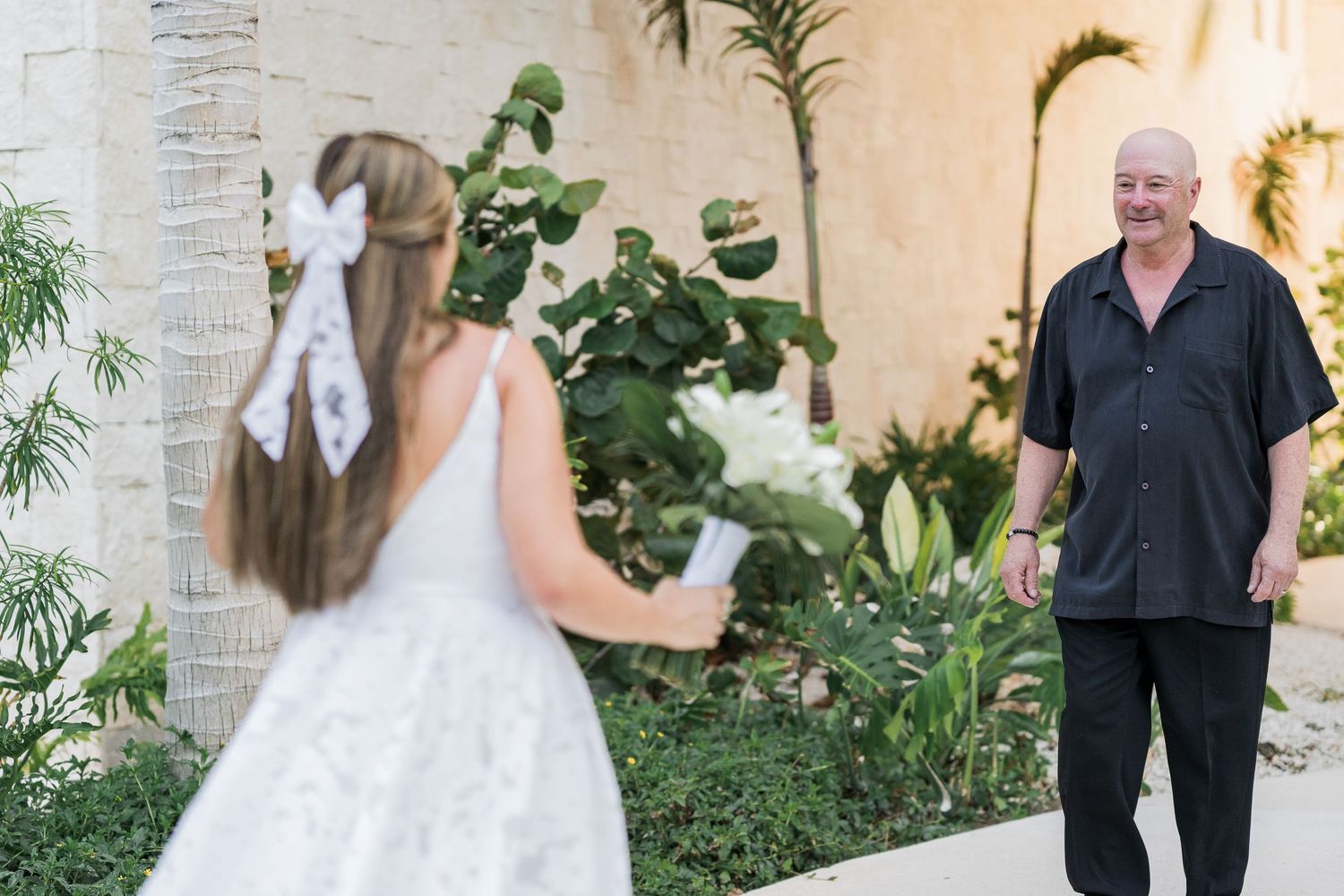 Bride in white gown shares emotional first look moment with older man in black shirt outdoors.
