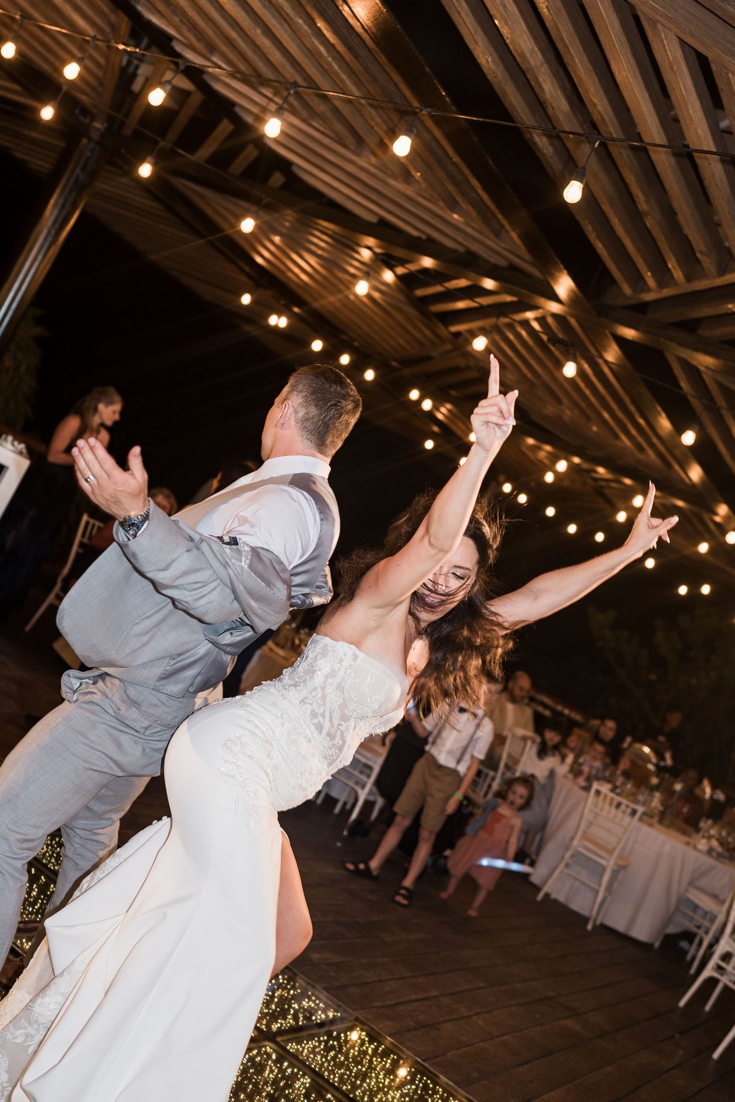 Bride and groom share joyful first dance under string lights at outdoor wedding reception.