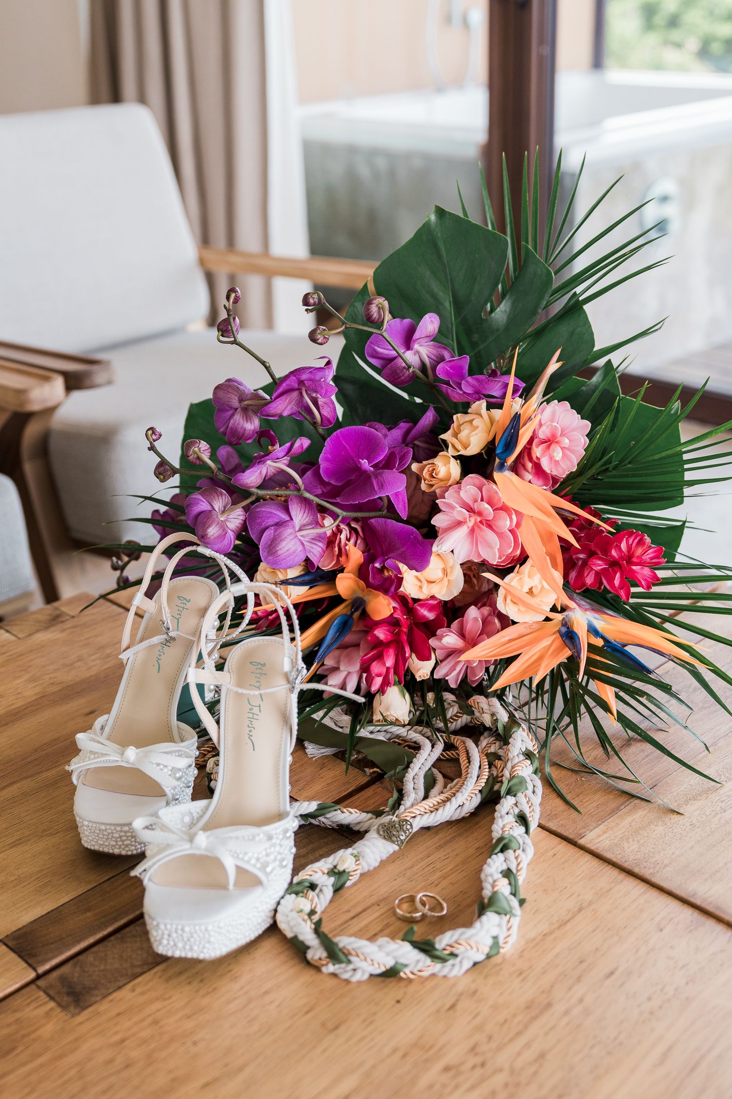 Hotel Xcaret México Wedding - bridal heels, tropical wedding bouquet with orchids and birds of paradise, and gold rings on a wooden table.