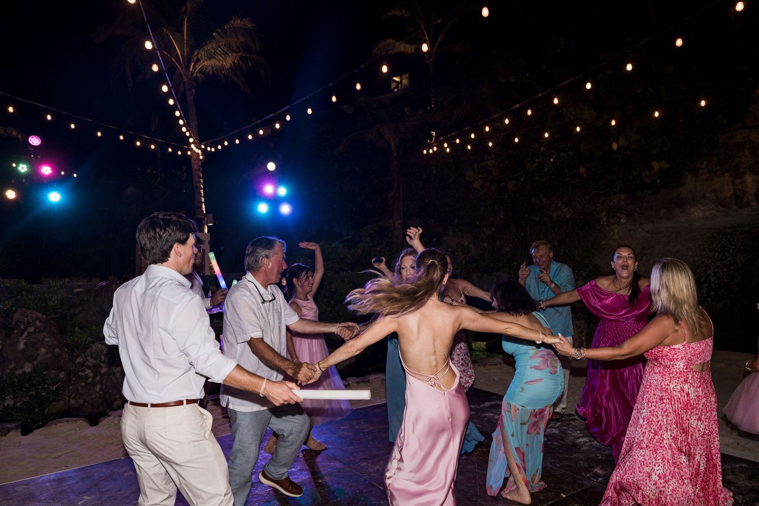 Hotel Xcaret México Guests dancing in a circle at an outdoor wedding reception under string lights at night.