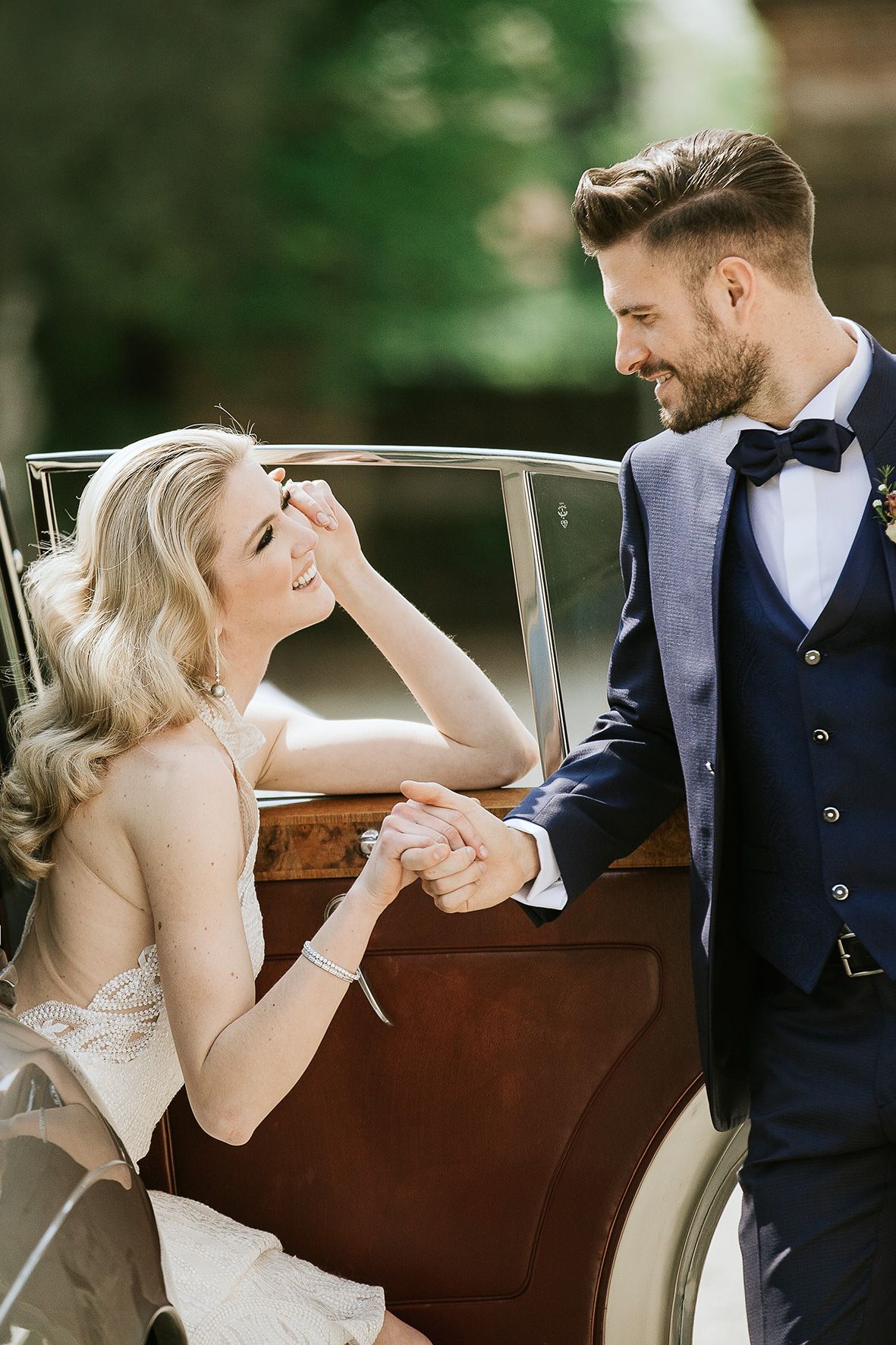 A happy couple share a tender moment beside a vintage car during their formal wedding photoshoot.