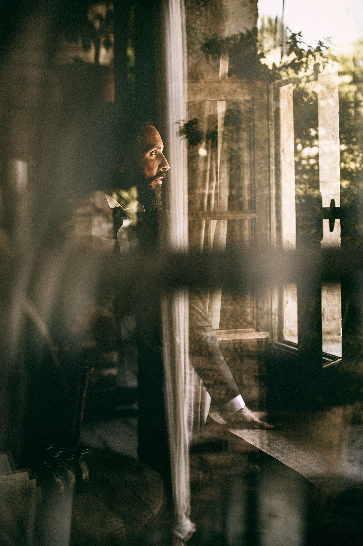 Through a window reflection, sunlight bathes a peaceful moment as someone gazes thoughtfully at the view.