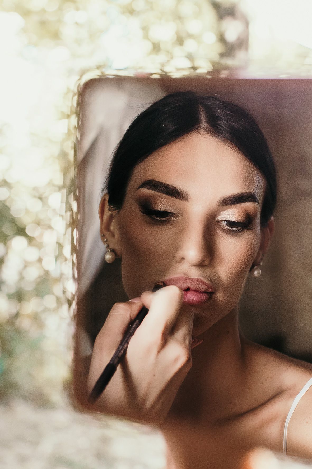 Close-up beauty shot showing lip makeup application with glowing bokeh light effects in background.