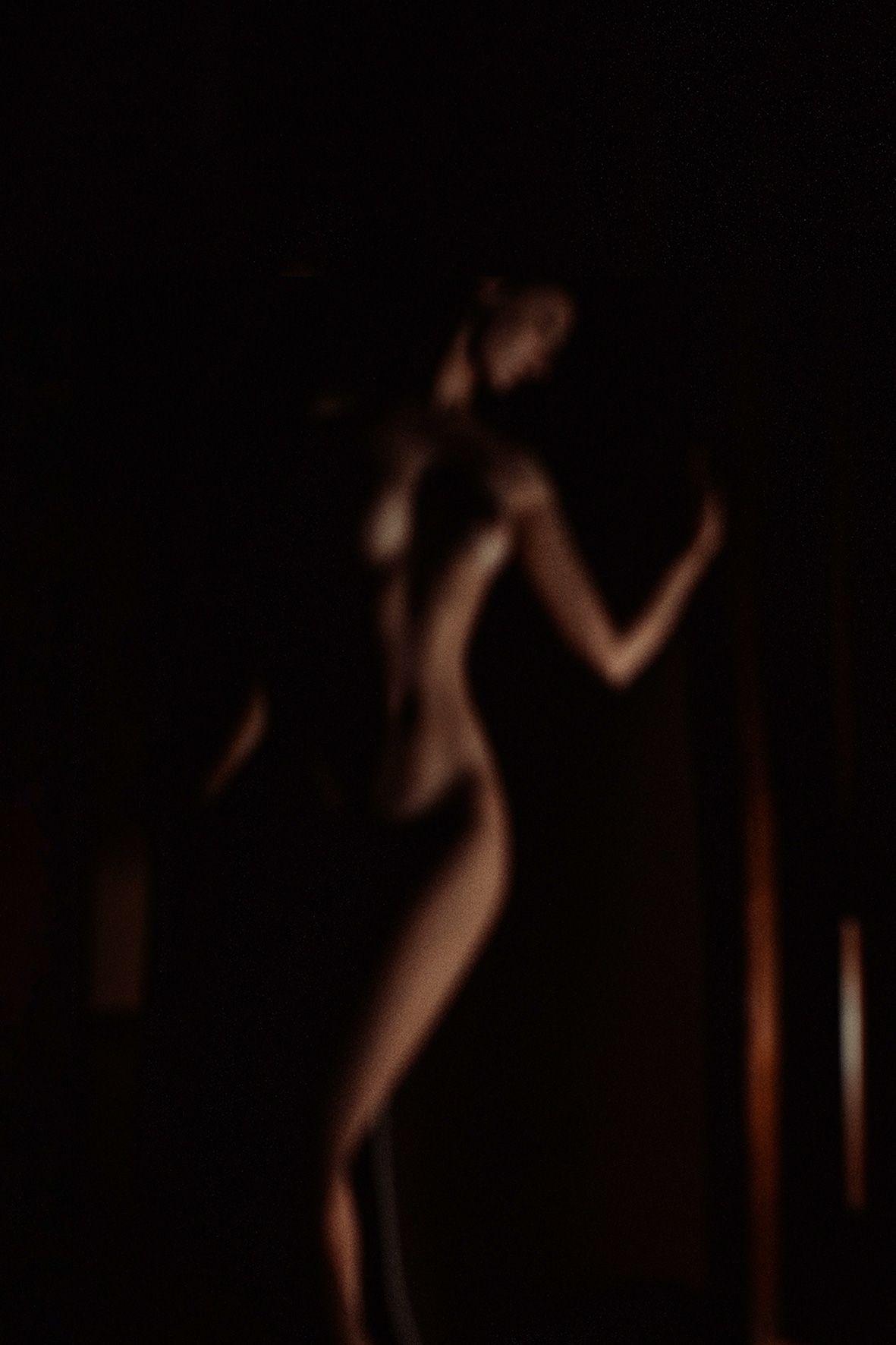 Artistic silhouette of a graceful female figure dancing in dark moody lighting with soft blurred edges.